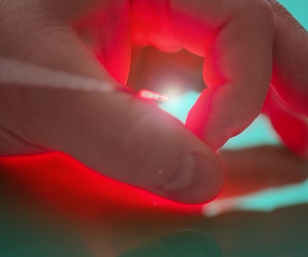 Source of bright light on the end the probe for treatment by means the laser between big and forefingers the left hand Source of bright light on the end of the probe for treatment by means of the laser between big and forefingers of the left hand of the person with reflection.