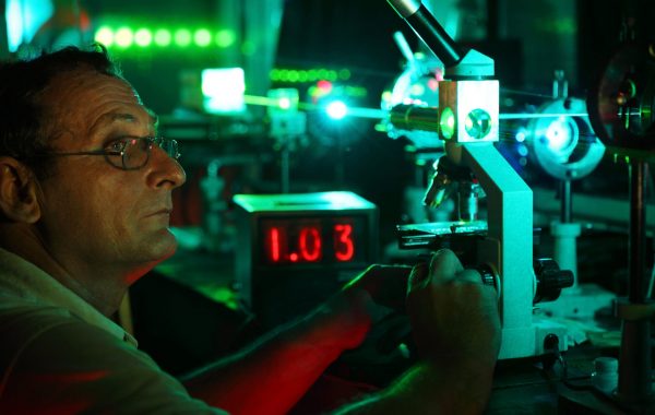 Scientist with glass demonstrate laser of microparticles near timer Scientist with glass demonstrate laser of microparticles near timer