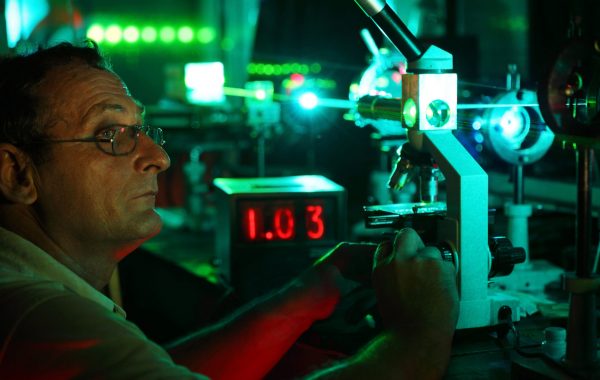 Scientist with glass demonstrate laser of microparticles near timer